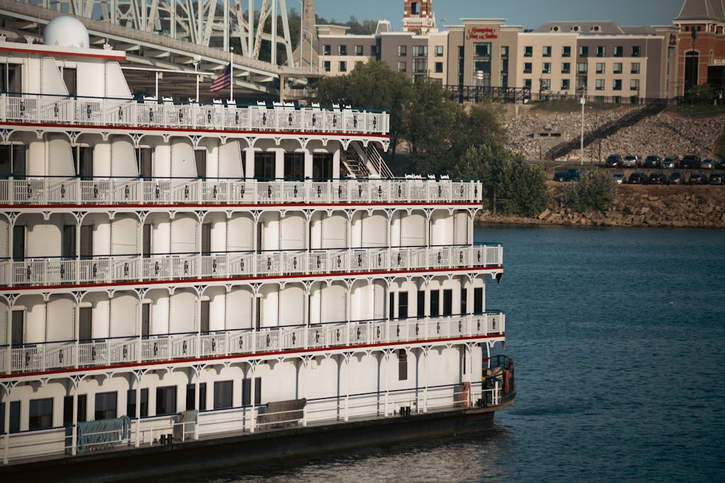A classic paddle steamer docked by an urban river with cityscape background.