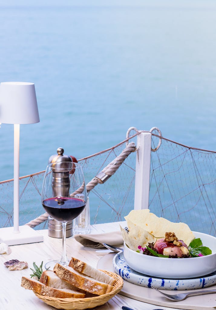 Elegant seaside dining with wine, salad, and bread on a nautical-themed table setting.