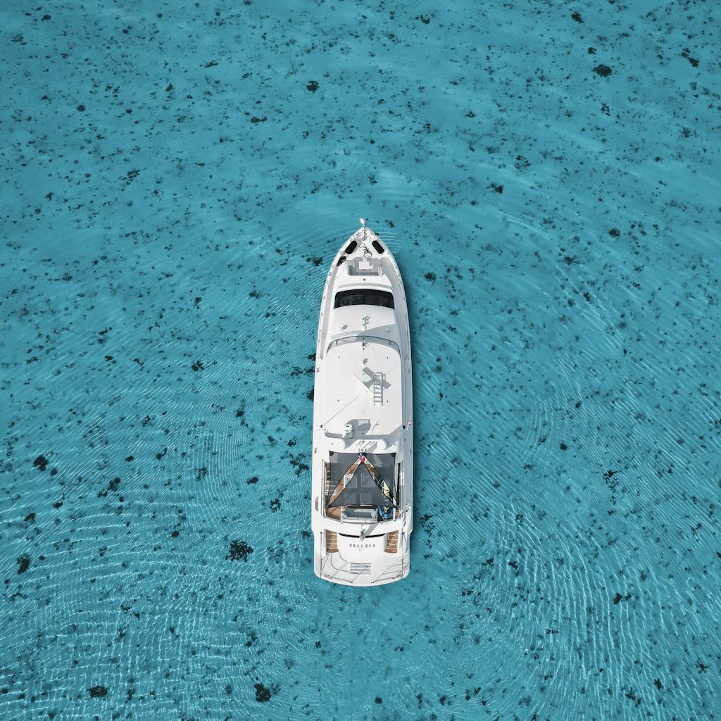 Top-down view of a white yacht in clear turquoise waters, surrounded by ripples.